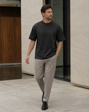 Man wearing the NORVEN Origin Heavyweight Tee in Charcoal with tailored trousers in a modern architectural setting