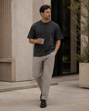 Man wearing the NORVEN Origin Heavyweight Tee in Charcoal while walking with coffee in a European architectural setting